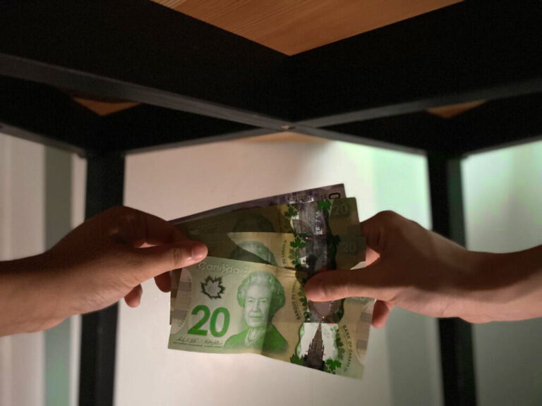 A hand reaches out under the table, handing over cash to another hand.