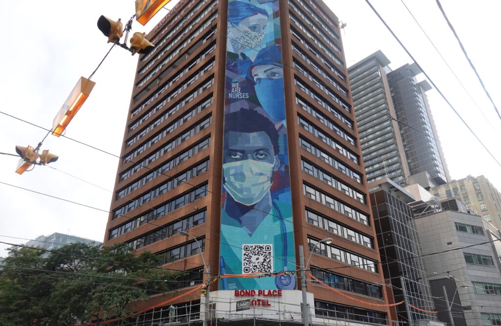 Outdoor banner on tall brick building of nurses wearing masks.