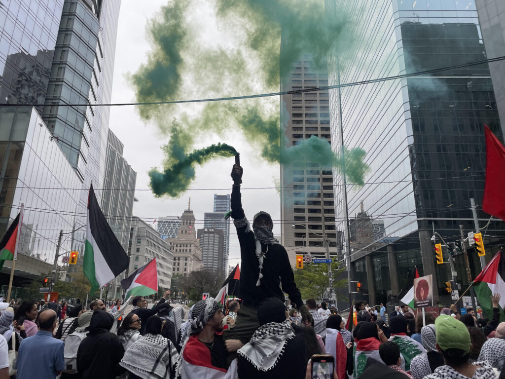 A photo of protesters and directly in the centre, a protestor holding a green smoke firecracker.