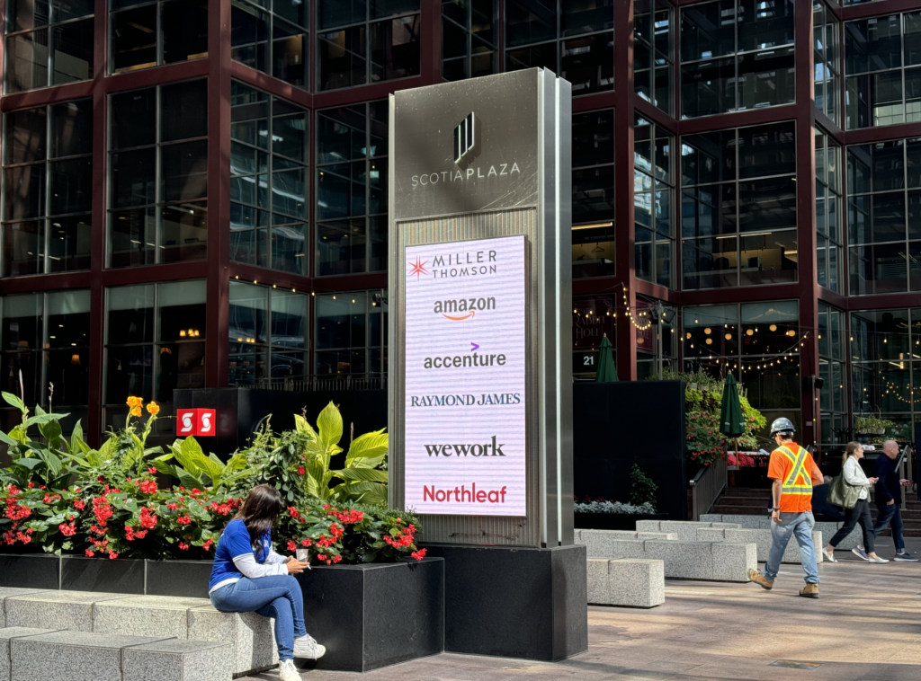 A landscape of the Toronto financial district, showing a directory panel of companies: Miller Thomson, Amazon, Accenture, Raymond James, We Work and Northleaf
