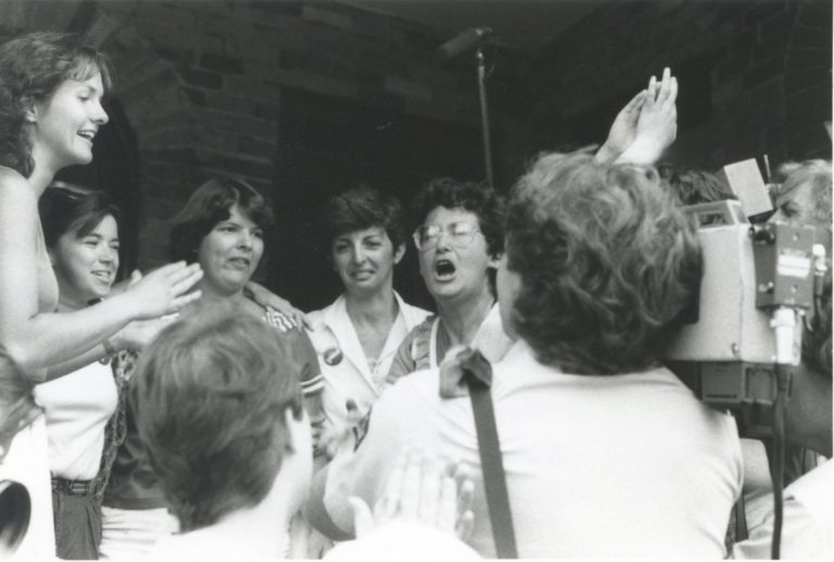 A black and white image of Rebick chanting amongst other women 