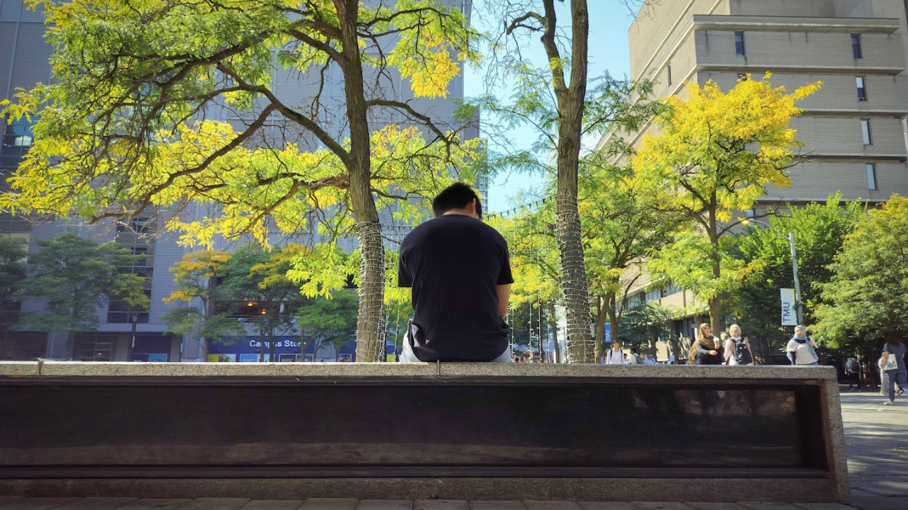 An individual sitting on an outdoor cement bench on TMU's campus looking down