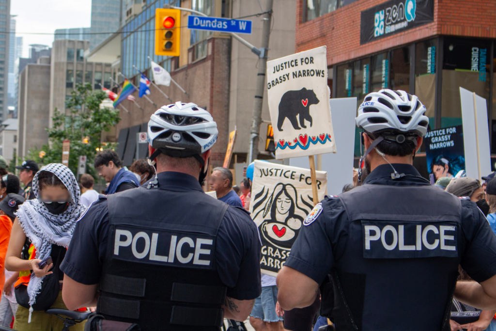 Police, signs reading "Justice for Grassy Narrows", A street sign "Dundas st. W."