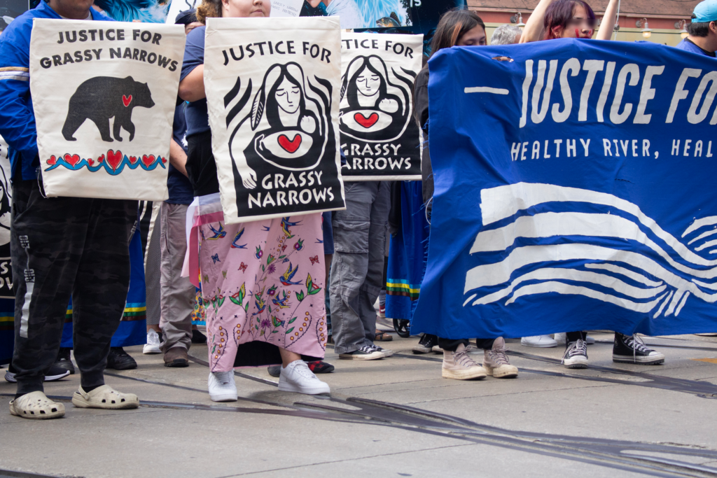 Protestors marching, signs reading "Justice for Grassy Narrows"