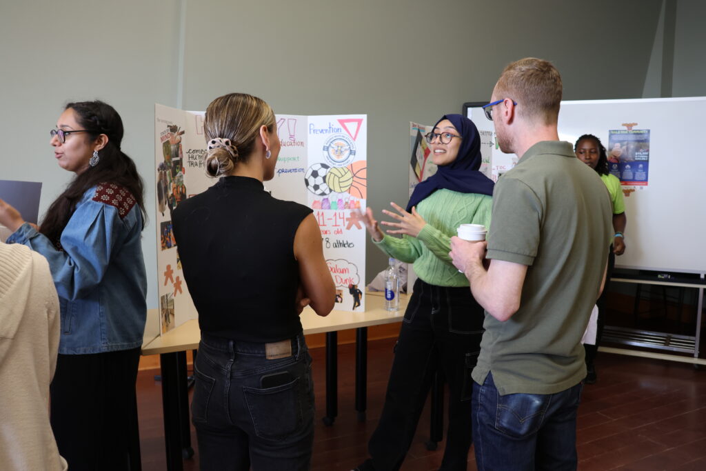 A woman stands in front of a board and explains something to two people standing in front of her.