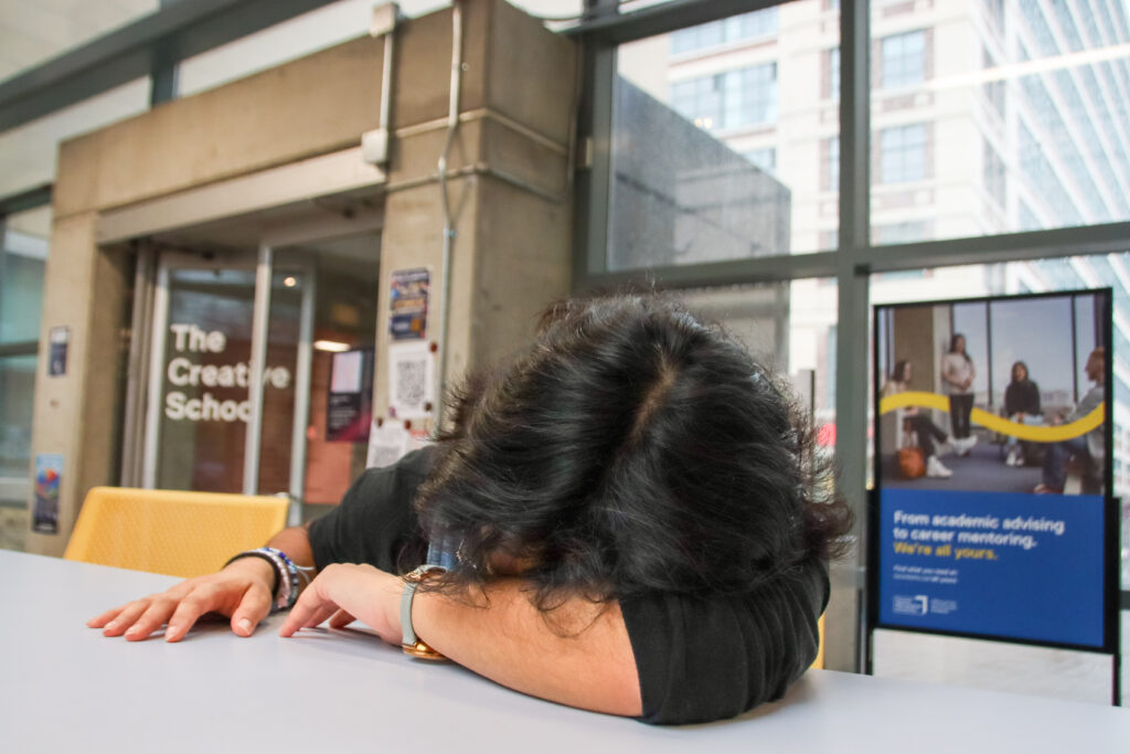 A student lies face down on a white table in a campus building