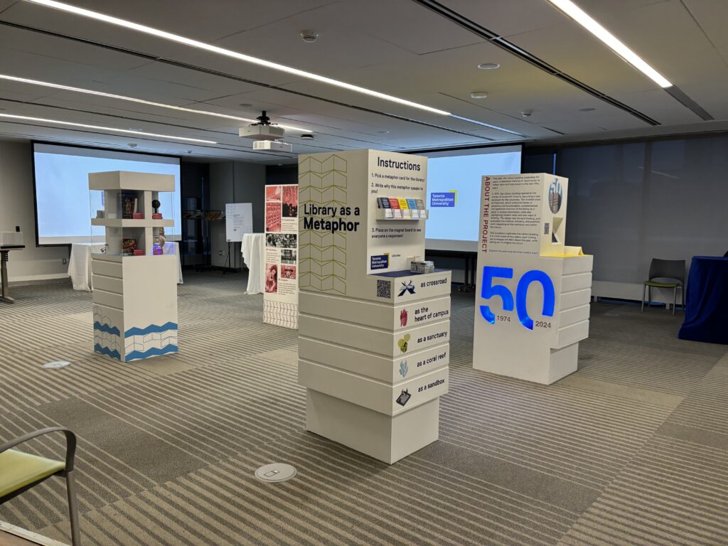 Four white structures with writing stand in a large room with a white board in the background 