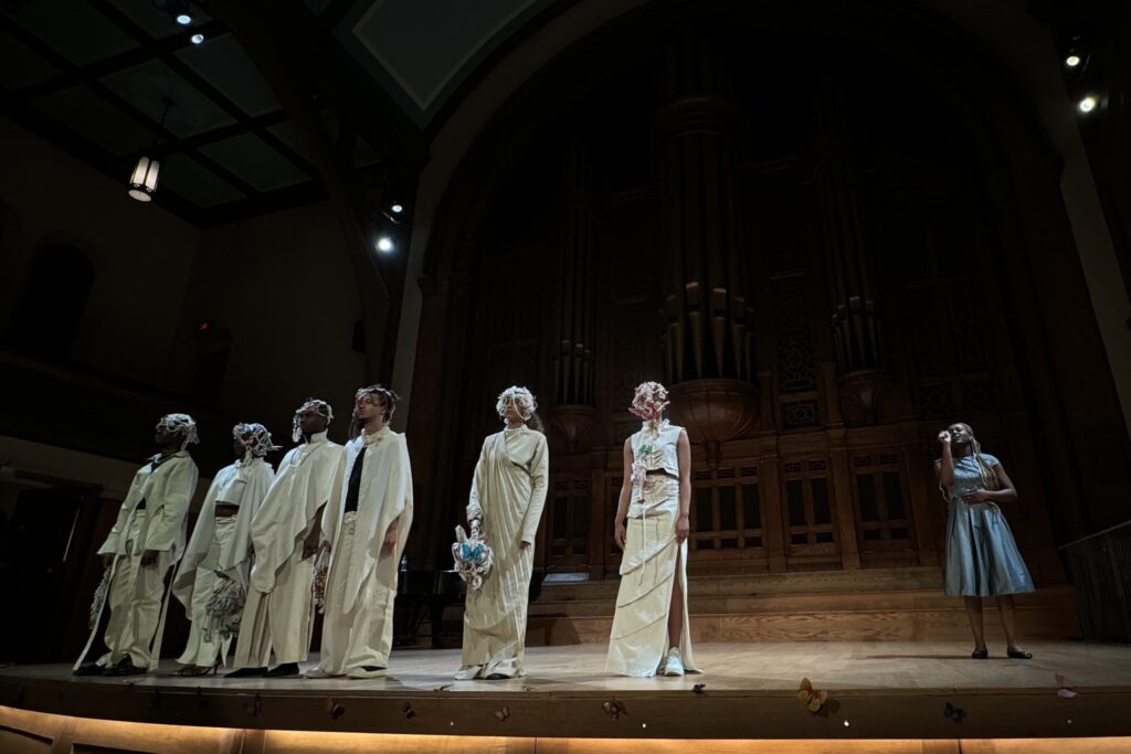 six models in white next to a woman singing on stage