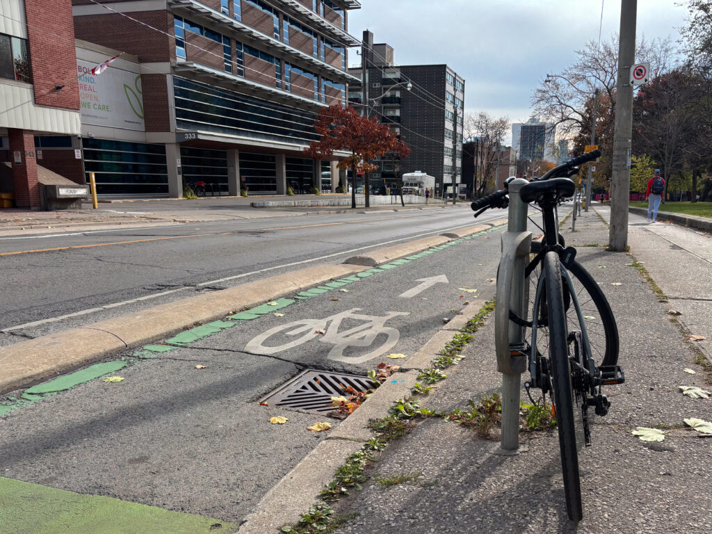 A black bicycle locked to a stand, right next to Sherbourne street's divided bike lane.