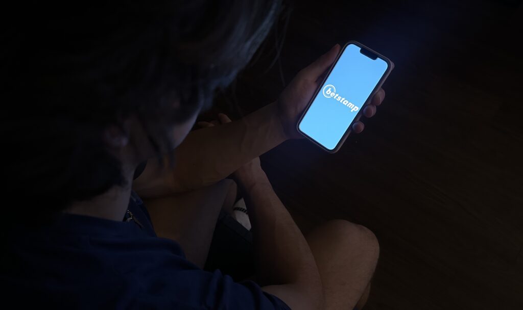 man holding phone with BetStamp logo on homescreen