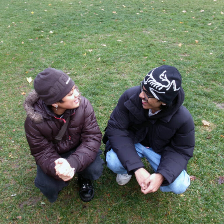 Two people kneeling and smiling at each other on a field of grass.