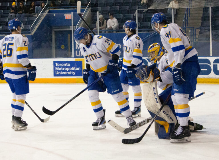 A bunch of hockey players on the ice wearing the blue, white and gold jerseys of TMU Bold.