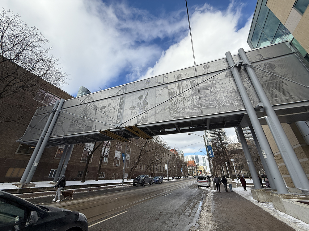 A photo of the bridge that spans Kerr Hall East to the Rogers Communications Centre taken from Church St. looking north with cars and snow on the road.