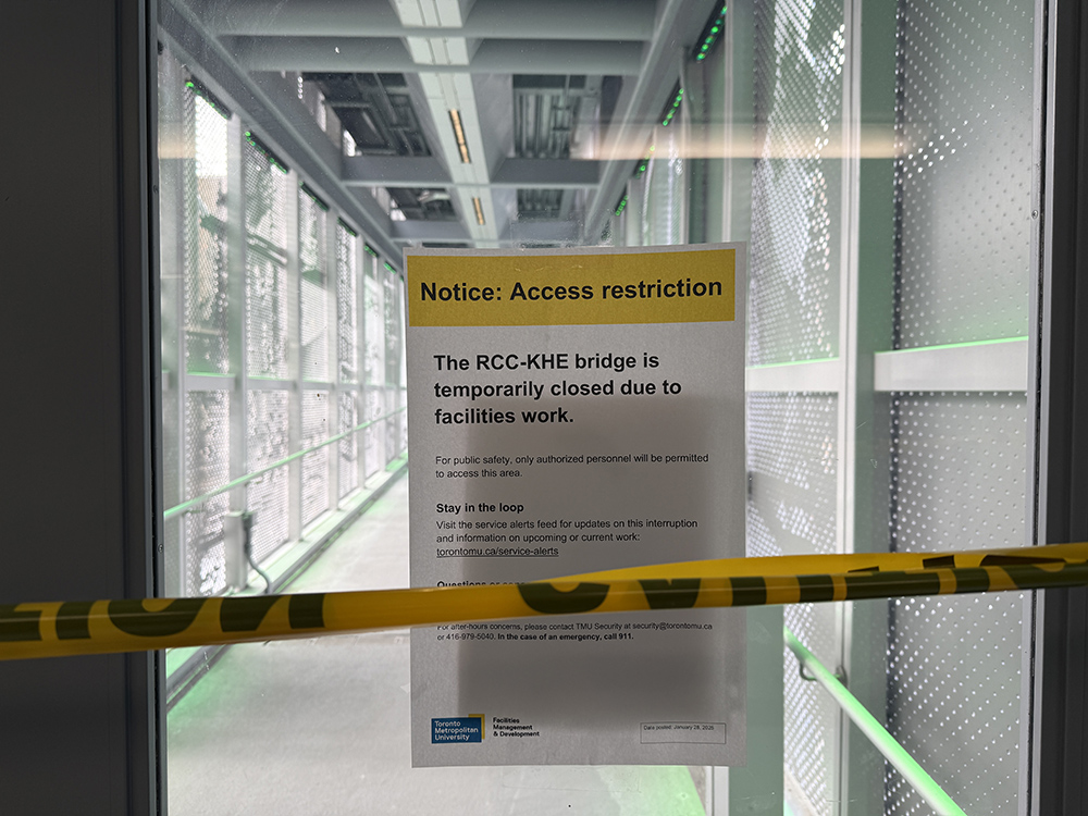 A photo of a sign posted on the door that leads from the RCC to the KHE bridge explaining that the bridge is closed, along with yellow warning tape.