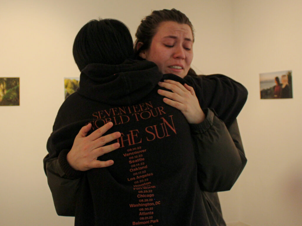 A crying person hugs someone wearing a black hoodie.