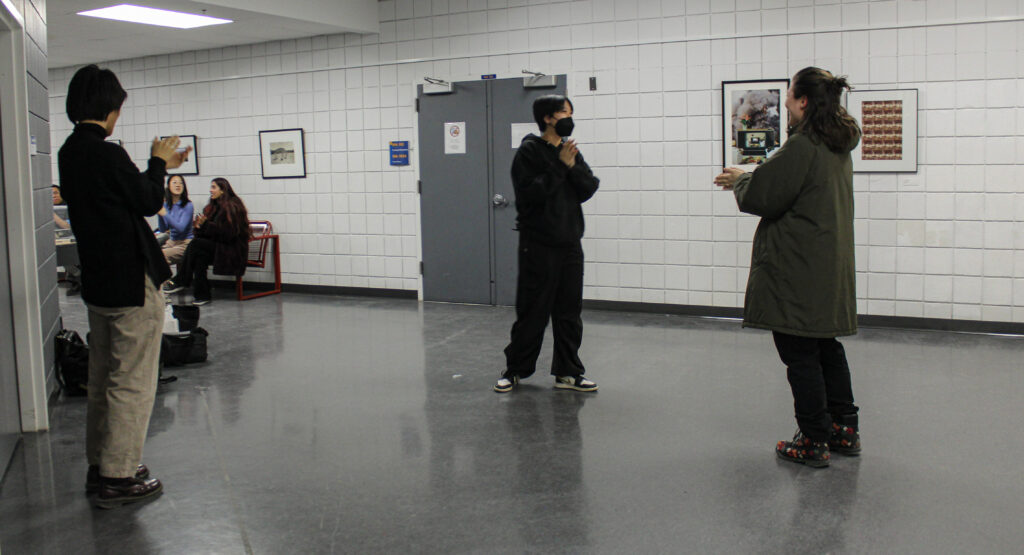 Five people clap for a person wearing a mask standing in the middle of the hallway.