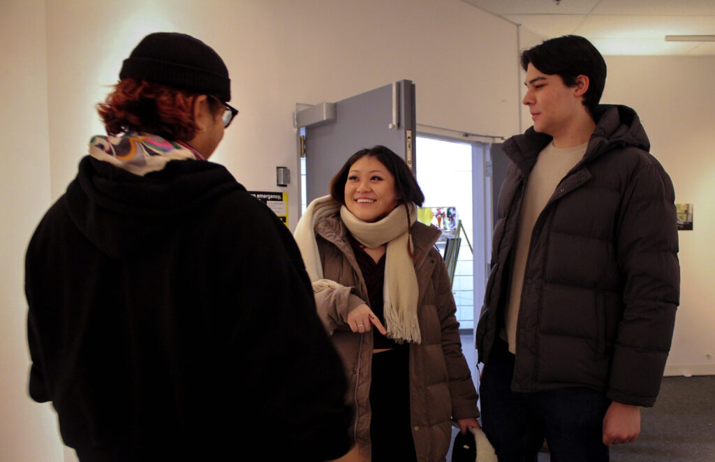 A smiling woman chats with two people inside a room.