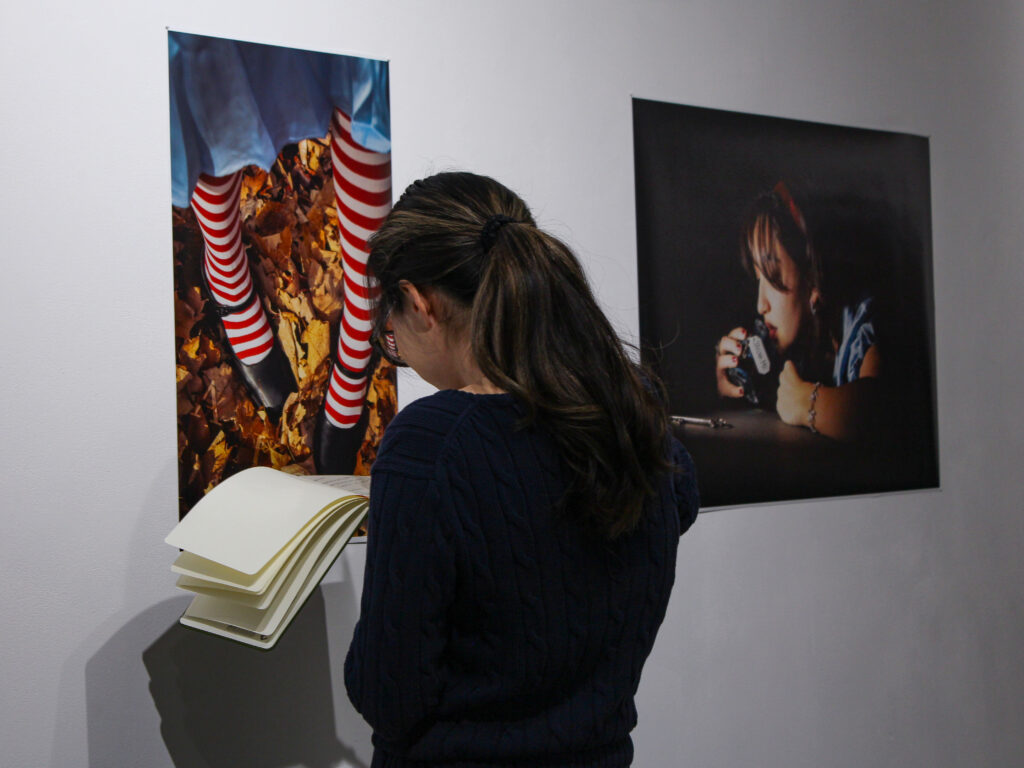 A girl with a ponytail writes into a notebook while facing a wall with photos hung up.