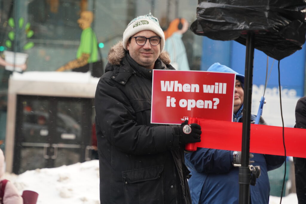 A photo of a rally-goer holding a red sign and a ribbon in front of the new Eglinton station.