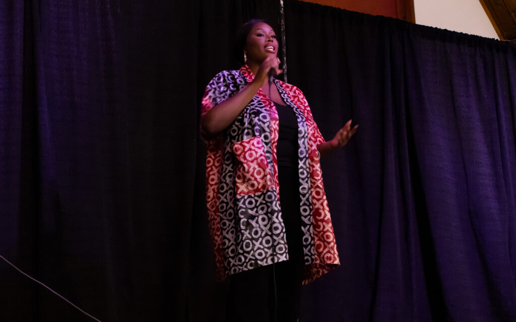 A woman in a blue and red robe sings into a microphone on stage