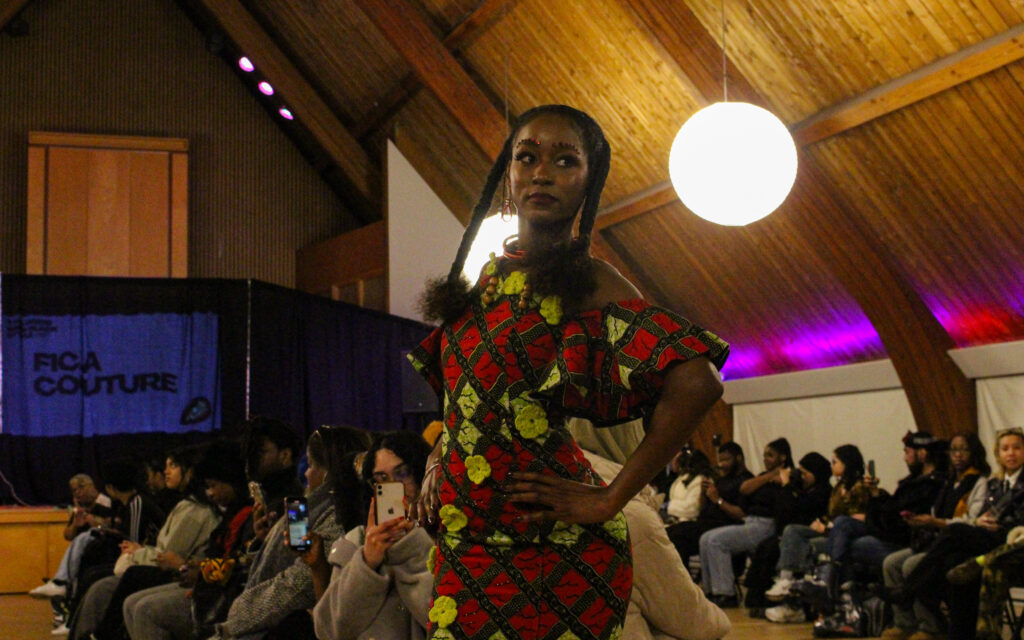 A woman in a patterned red and yellow dress poses at the end of a runway