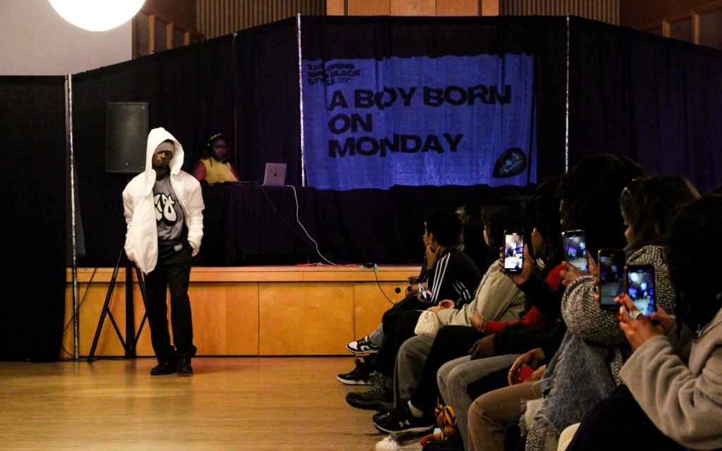 A man in a white hoodie and black pants poses on the runway