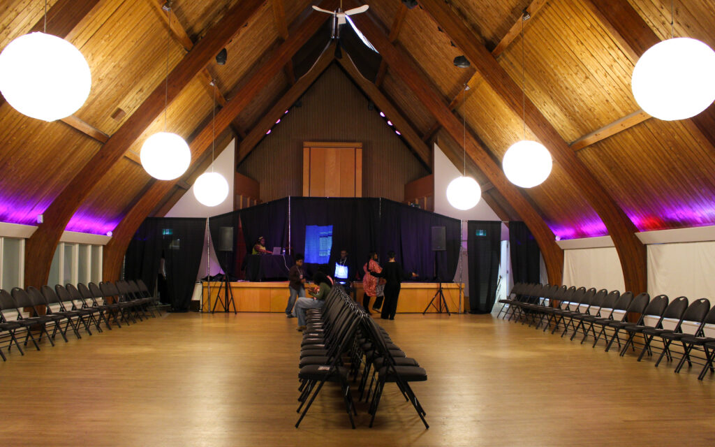 An room with wooden panels and cathedral ceilings with four rows of chairs lined up