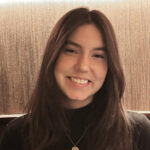 A photo of a woman with long brown hair, smiling, sitting at a restaurant.