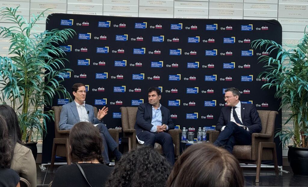 Martin Regg Cohn, Dr. Hossein Rahnama, and AI Minister Evan Solomon sitting on three chairs, on a podium, with a black background behind them, which displays the TMU and the dais logos.