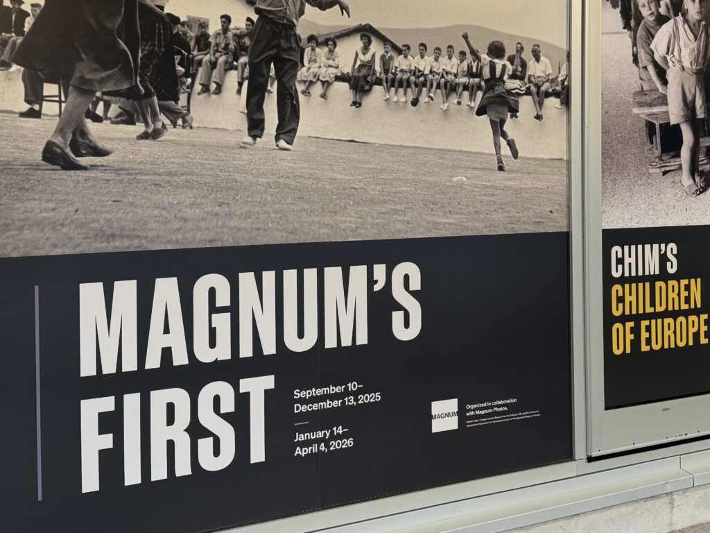 A sign at the front of The Image Centre announcing the opening of the "Magnum's First" exhibition featuring black and white photos of the art.