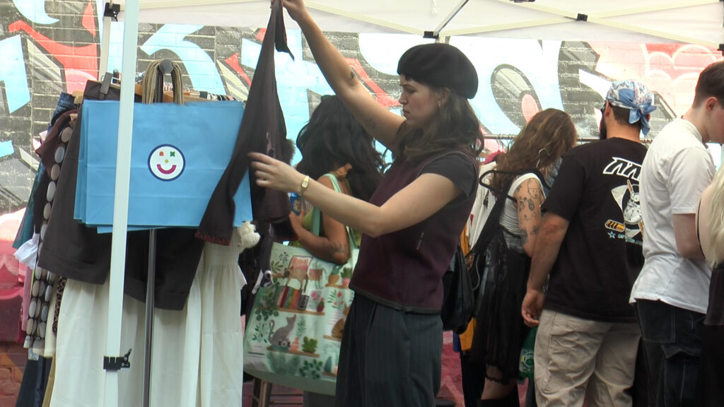 Amodio-QueenWest This is a photo of a woman looking through clothes at Good Friends Market with a crowd behind her.