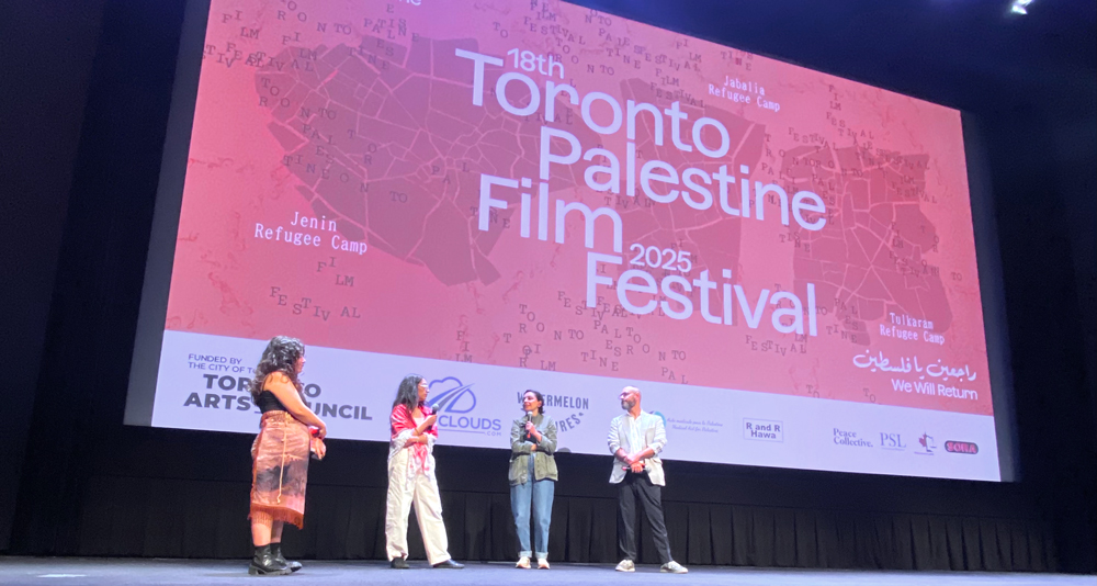 A photo of four filmmakers standing on the stage, with the logo for the TPFF behind them on the movie screen.