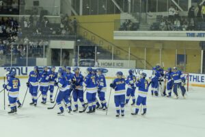 A photo of 19 hockey players on the ice giving each other high-fives after their homecoming win in front of a packed crowd.