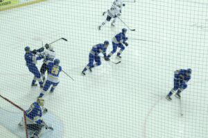 A bird’s eye view of hockey players in blue and white scattered on the ice, fighting for the puck.