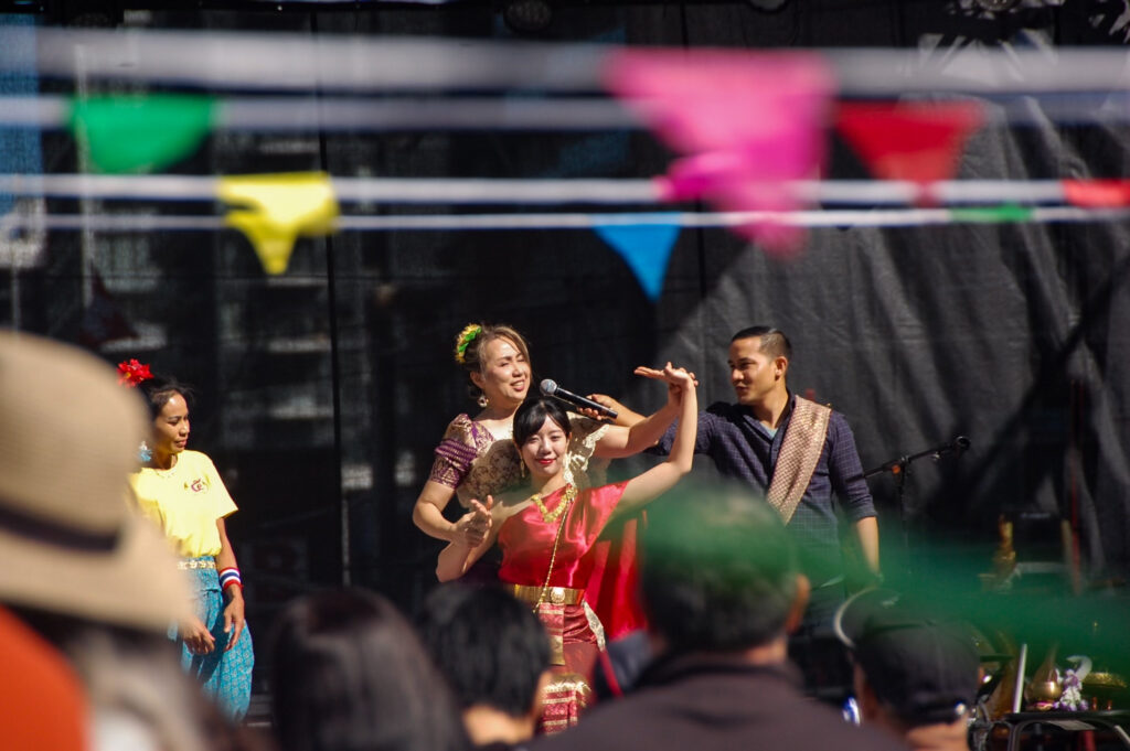 A photo of a woman with a microphone adjusting a woman performing with a man standing behind. They are on a stage.