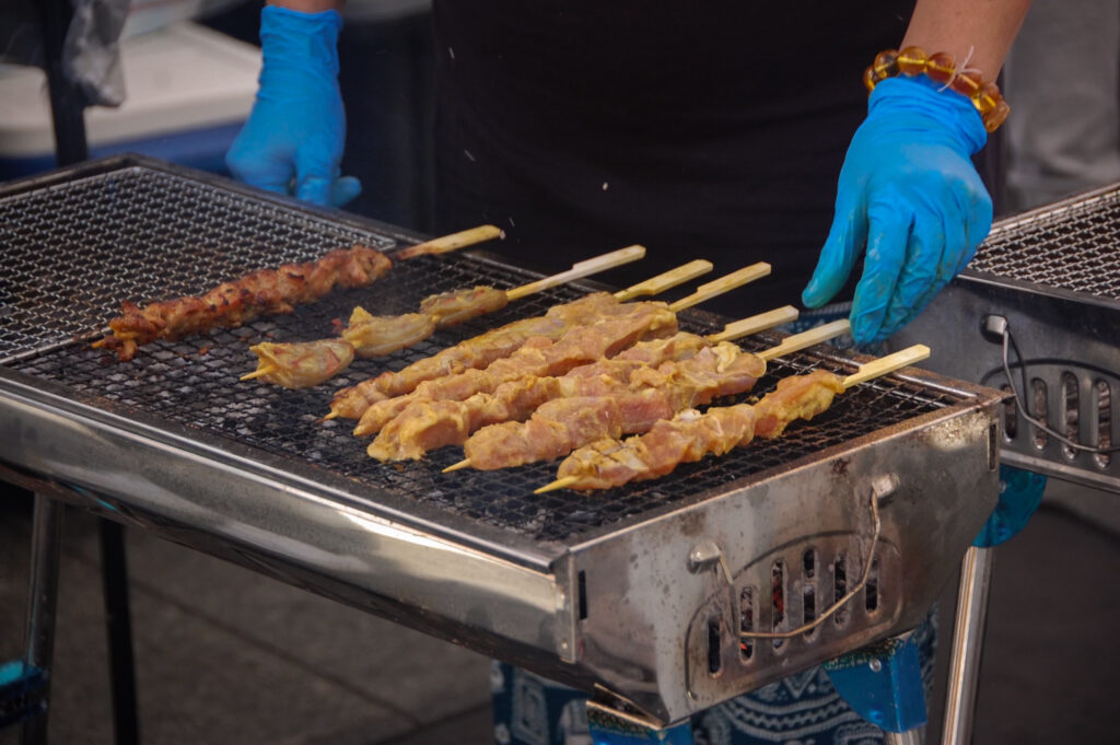 This is a photo of raw pork skewers being cooked on a grill. There is one skewer more cooked than others.
