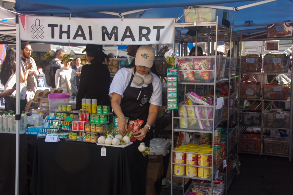 This is a photo of the Thai Mart booth. A woman stands behind adjusting something being sold.