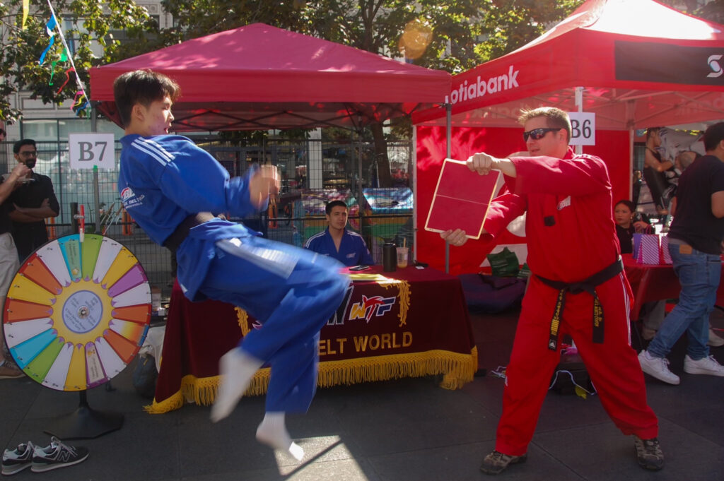 This is a photo of two people doing taekwondo, the teacher is holding a board while the student kicks.