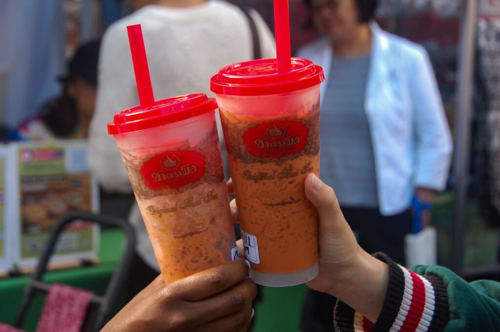 This is a photo of two hands holding Thai tea with a red lid and a red straw.