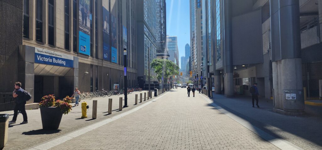 TMU's Victoria Building is on the left, and students are walking along the street.