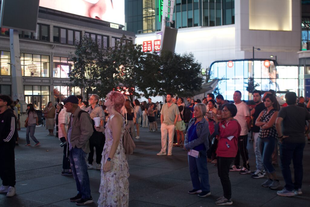 A group of people on Sankofa Square looking at the "Disappearing Acts" Nuit Blanche installation