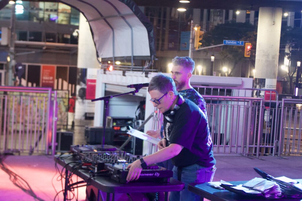 DJs Denise Benson and John Caffery at a DJ table, playing for the "Disappearing Acts" Nuit Blanche installation.