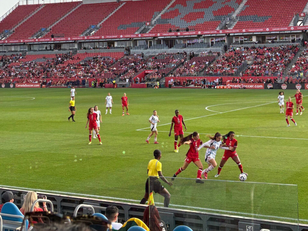 A group of women in red and white uniforms playing soccer in a stadium field.