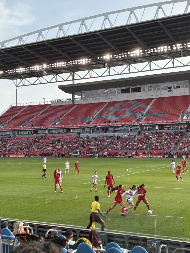 A group of women in red and white uniforms playing soccer in a stadium field.