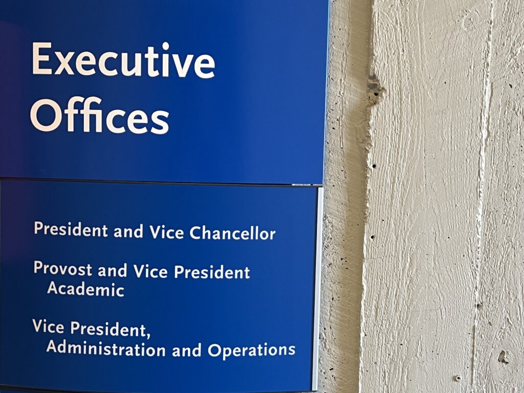 A photo of a blue sign for the executive offices at TMU in Jorgenson Hall.