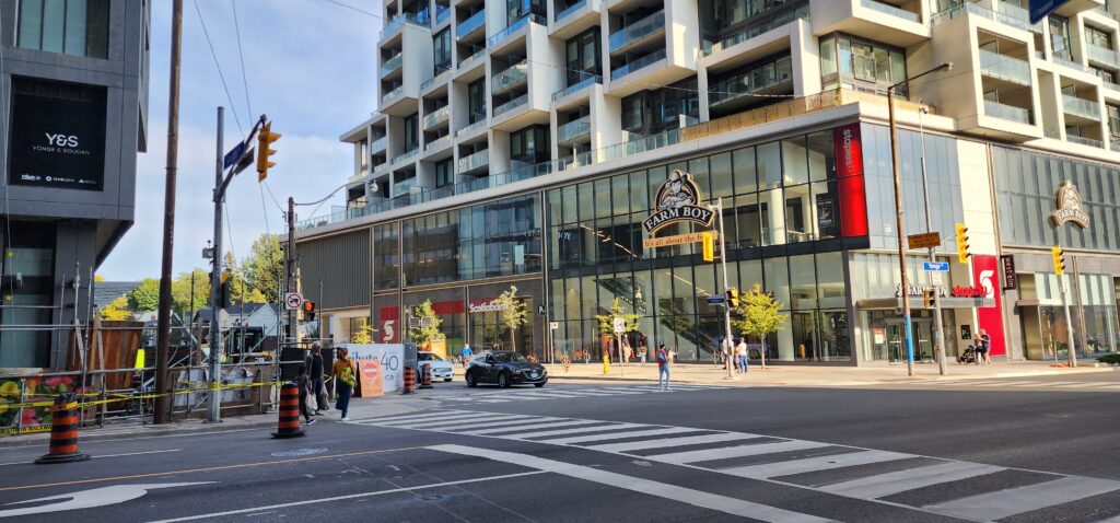 Street-level view of Yonge and Soudan in midtown Toronto, showing a Farm Boy grocery store and surrounding construction barriers beneath a new condominium building