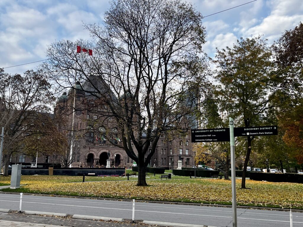 Provincial Legislative building on a university campus with the Canadian flag, trees, and directions of the campus
