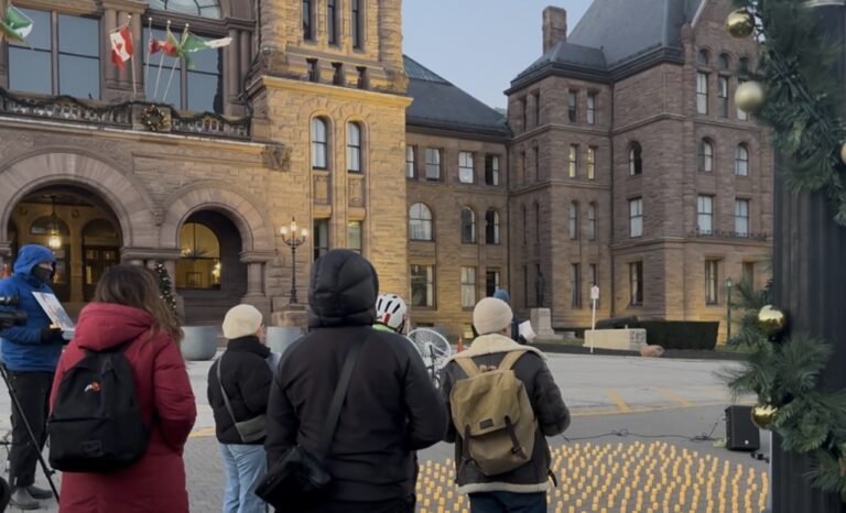 A group of people standing around candles lined on the ground in front of a building.