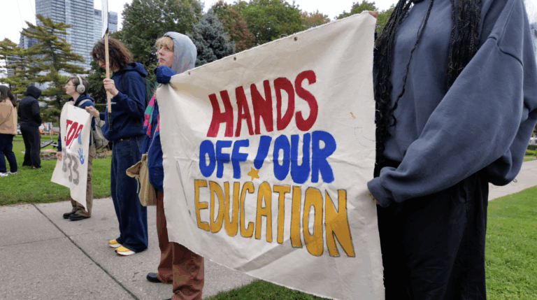 Protesters hold up a painted banner that reads “HANDS OFF OUR EDUCATION”.