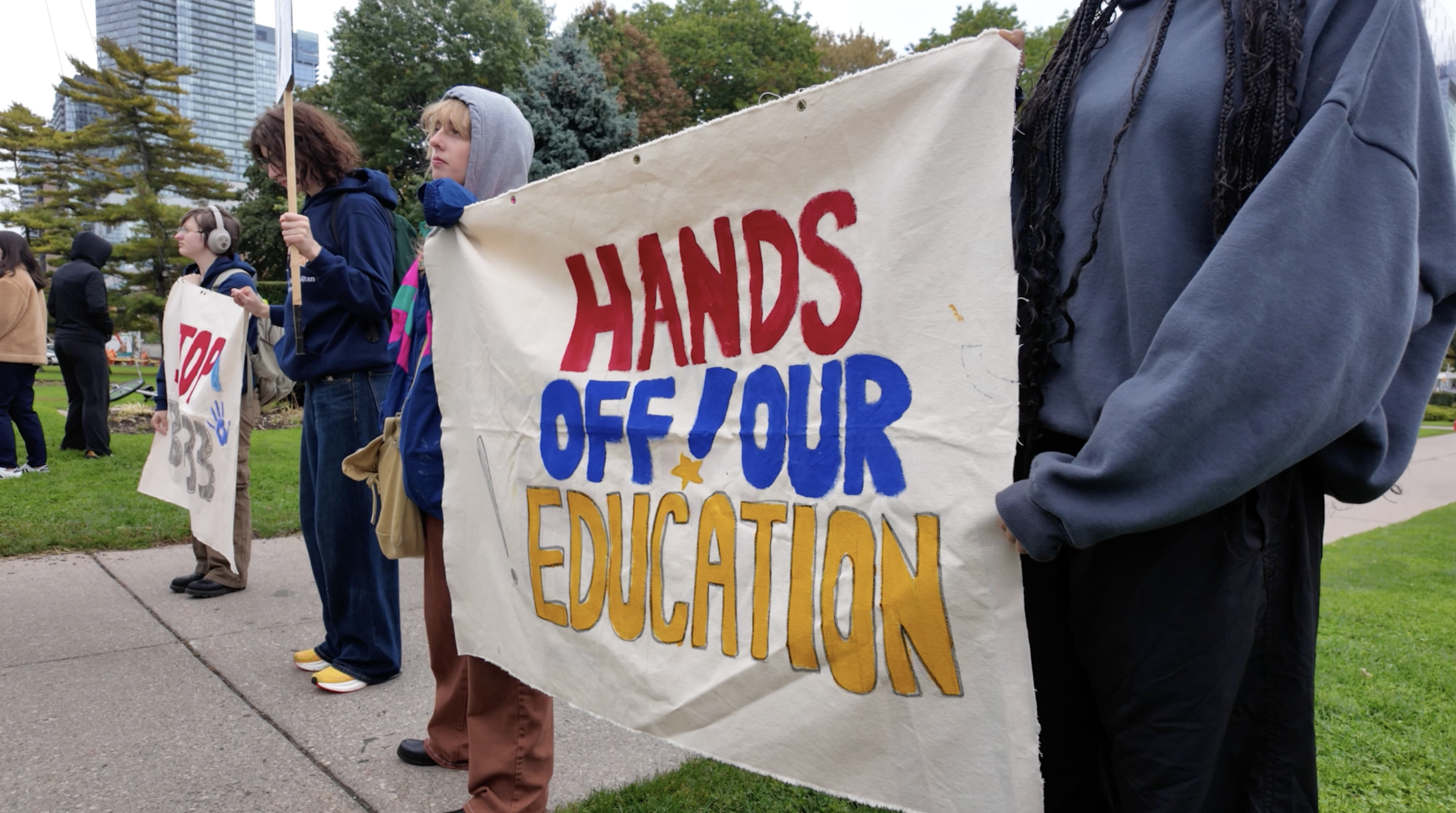 Protesters hold up a painted banner that reads “HANDS OFF OUR EDUCATION”.